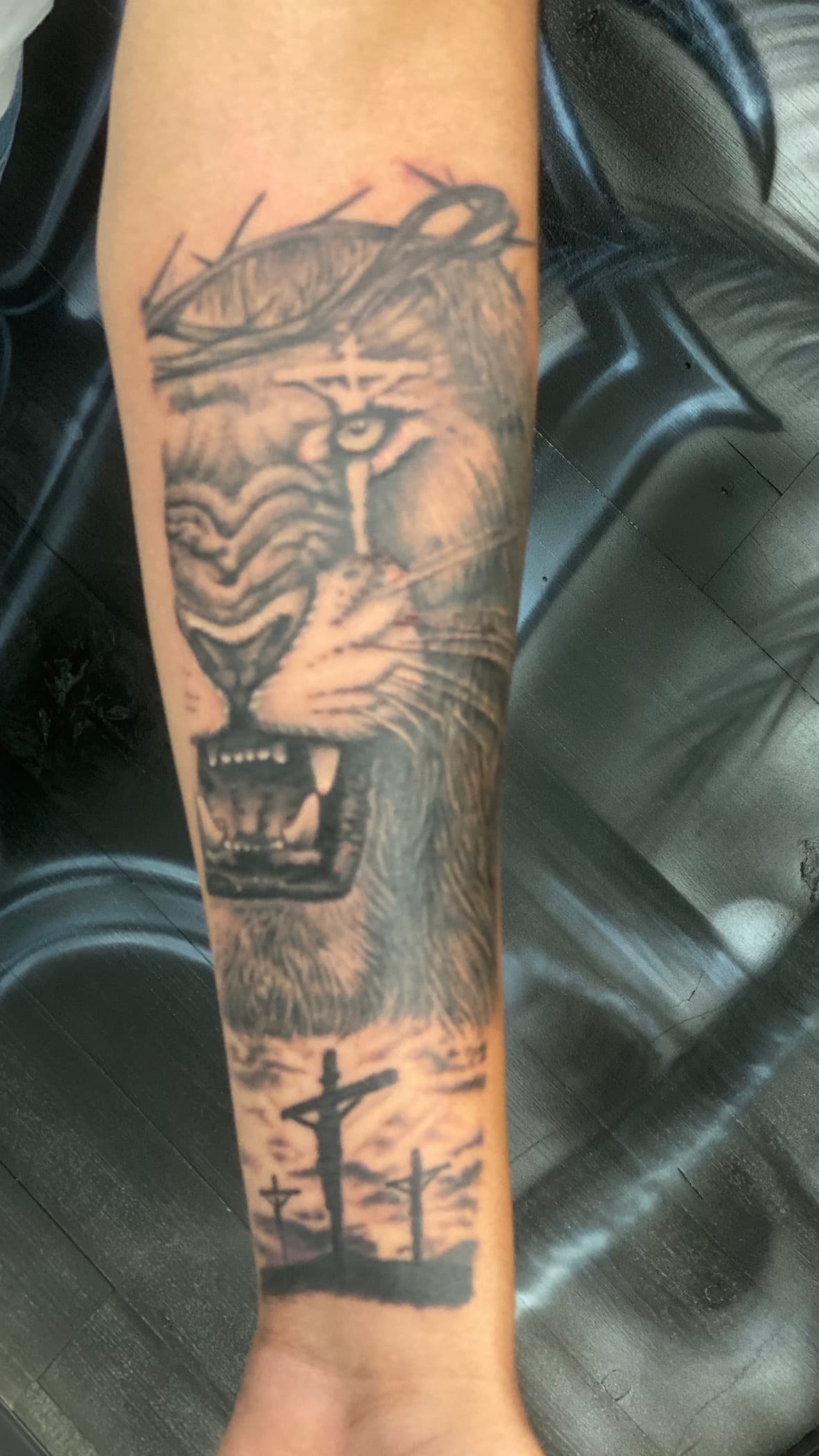 Black and grey realism tattoo of a lion's face crowned with thorns above three crosses on a hill, religious design by Isaac Mackenzie at TNT Tattoo, Aiea, Oahu